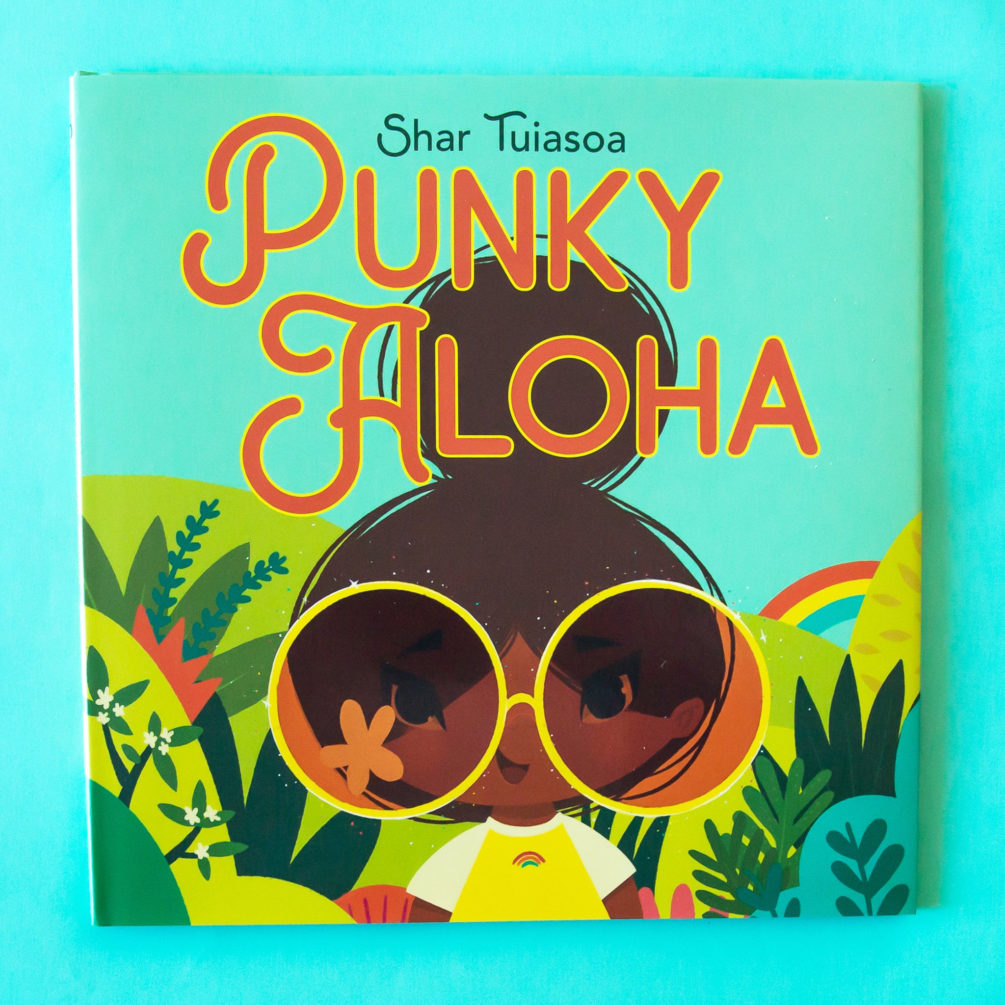 A vibrant book cover with the main character in a groovy rainbow tshirt and big round sunnies along with the title that reads, &quot;Punky Aloha&quot;.