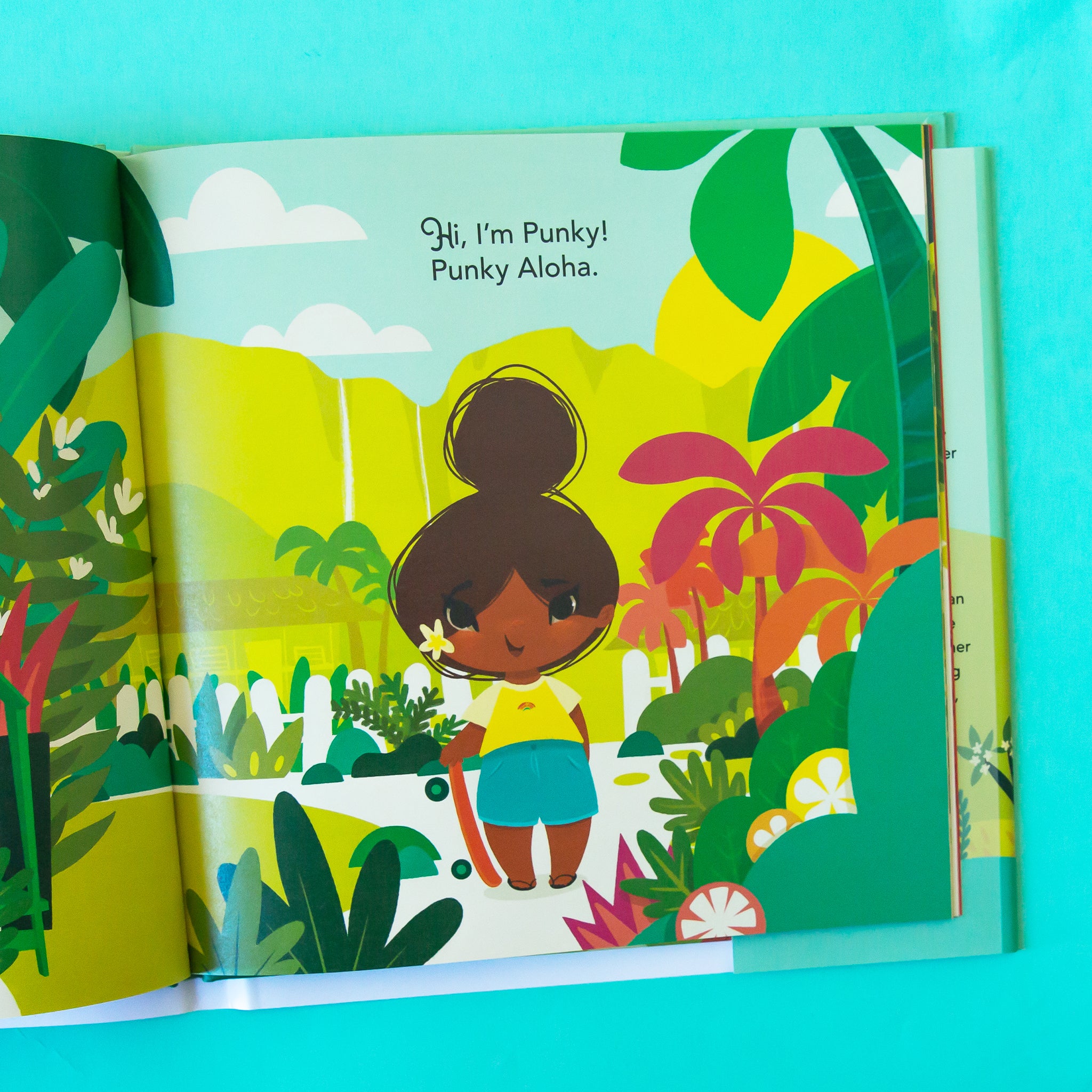 A vibrantly illustrated book opened to a page with illustrations of the main character Punky with a skateboard and text above that reads, &quot;Hi, I&#39;m Pinky! Punky Aloha.&quot;. 