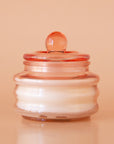 Peach colored translucent glass beam candle vessel with white wax and matching glass lid.