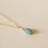 On a neutral background is a gold chain necklace with a blue Aquamarine stone at the center. 