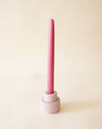 On a neutral background is a light purple ceramic candle holder with a magenta shade taper candle sold separately.