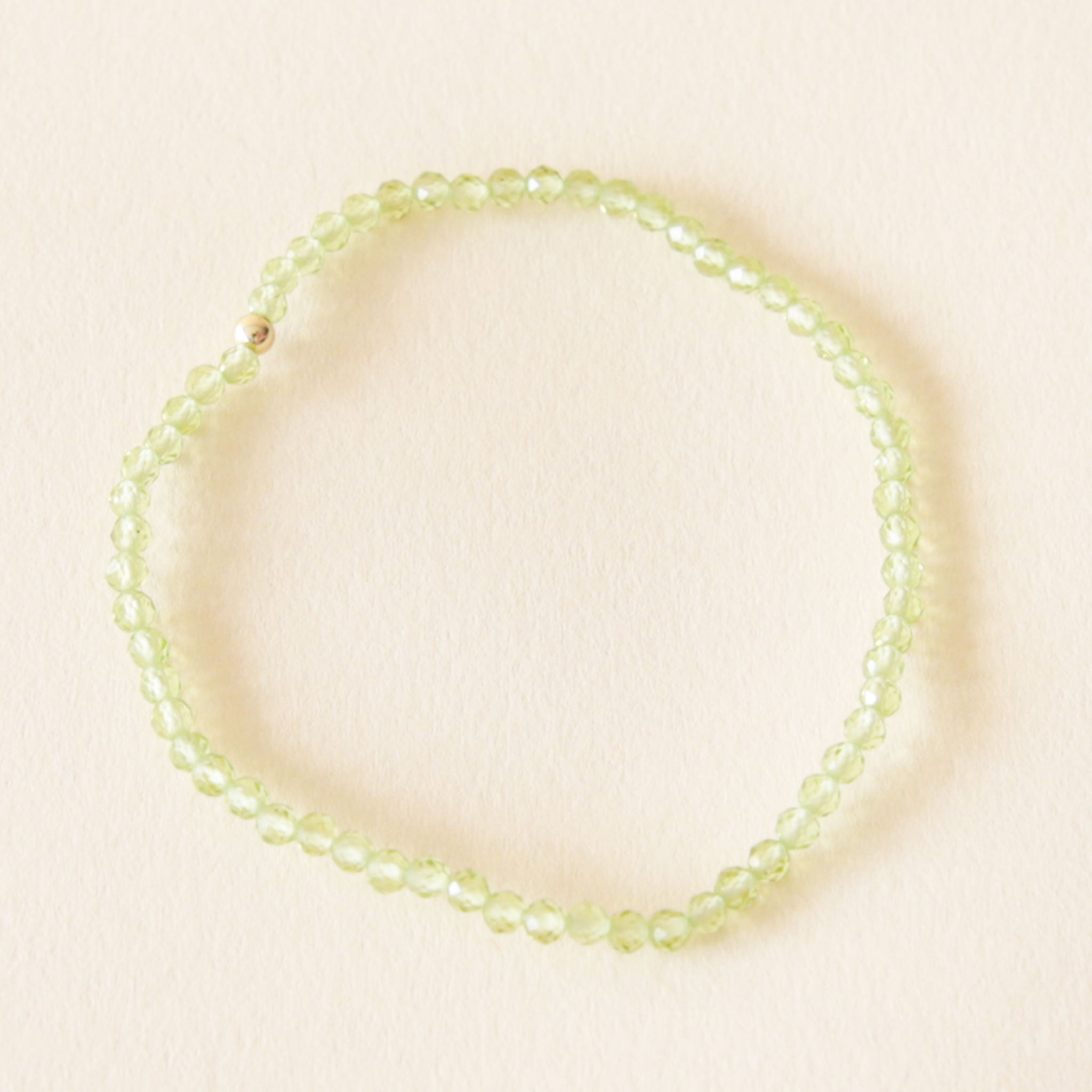 On a neutral background is a light green Peridot bead bracelet with a single gold bead in the center. 