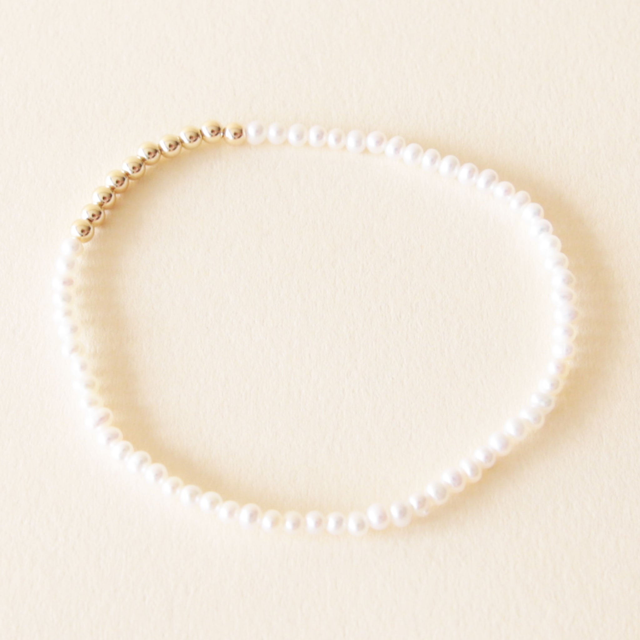 On a neutral background is a gold bead and pearl bracelet. 