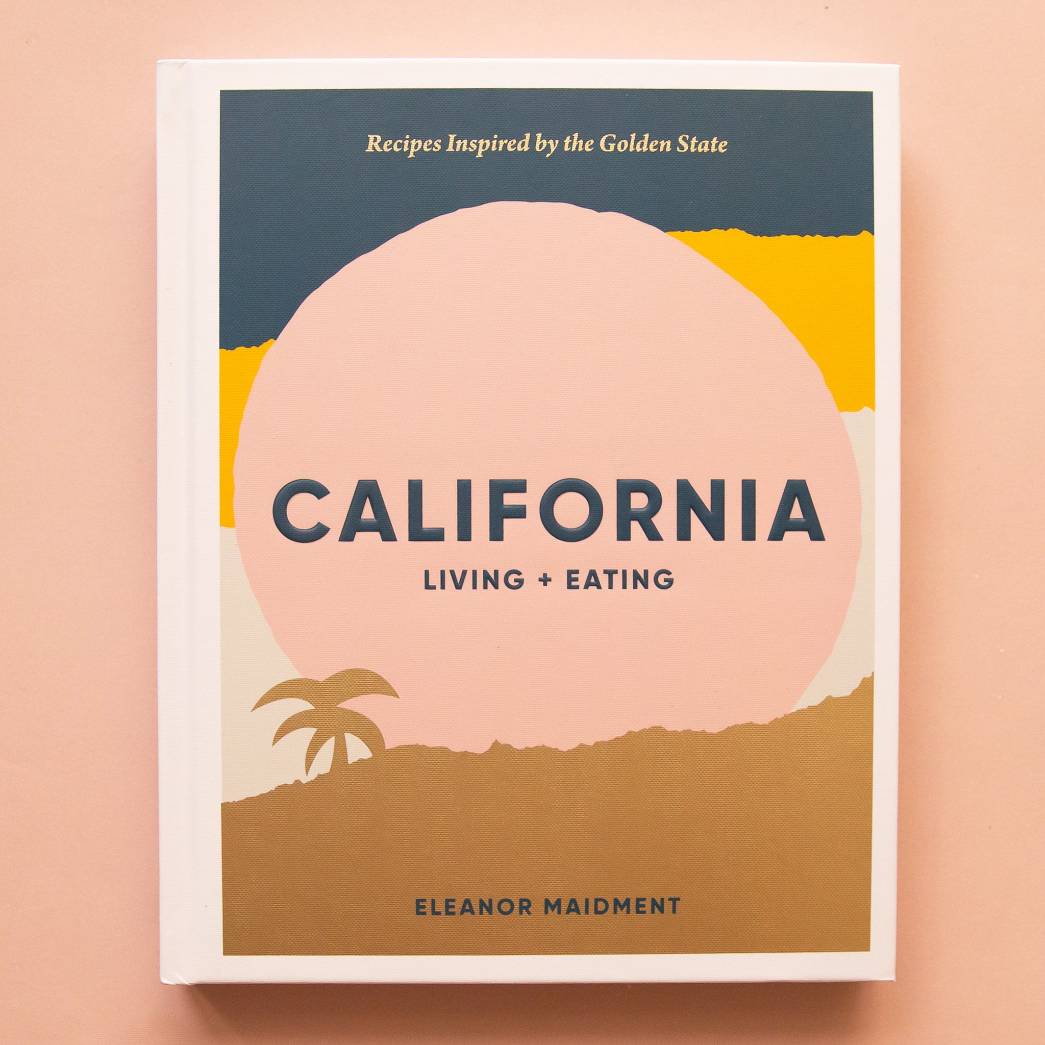 On a tan background is a blue, pink and yellow book cover with the title in the center that reads, &quot;California Living + Eating&quot;. 