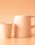 On a neutral background is a ceramic mug with an infuser cup to insert inside the rim of the mug.