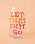 On a peach background is a drinking glass with red, pink and orange words on the front that reads, "Let That Shit Go".