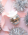 On a pink background is a disco ball car charm with a white cowboy hat and a string for hanging.