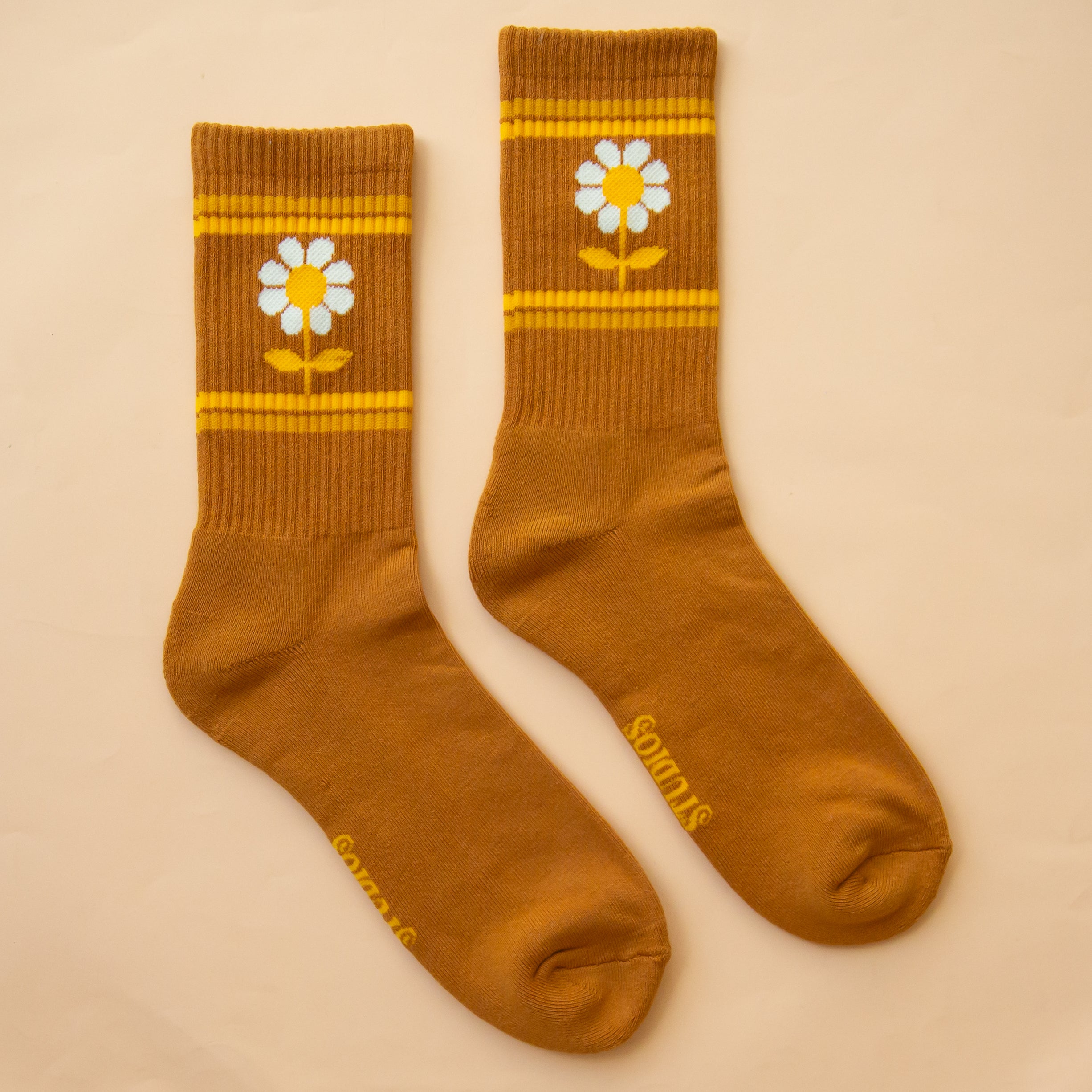 On a peachy background is a burnt orange pair of socks with a daisy graphic on the sides. 