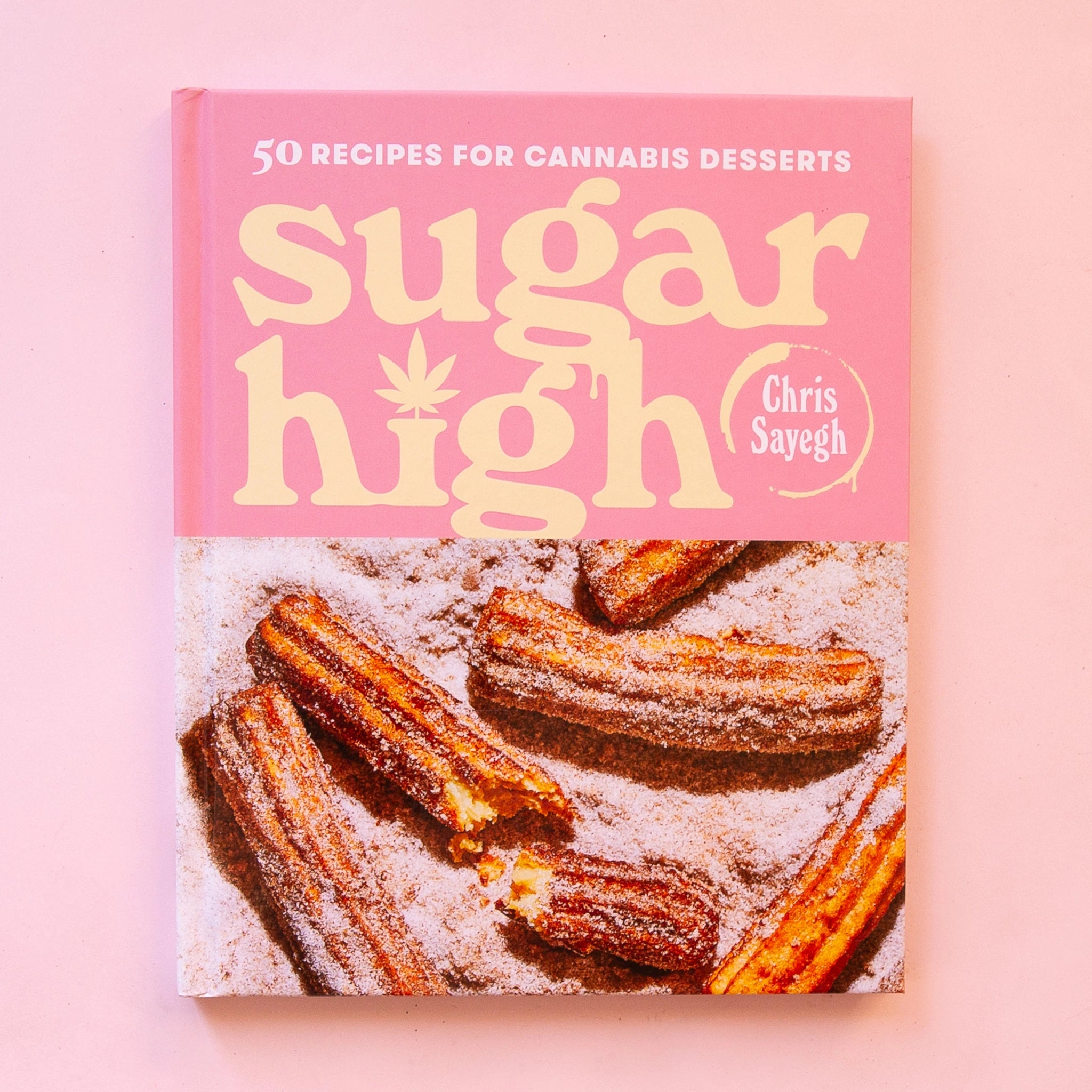 A pink book cover that reads, &quot;50 Recipes for cannabis desserts Sugar High&quot; along with the bottom half that features a photo of sugar churro.