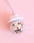On a pink background is a disco ball car charm with a white cowboy hat and a string for hanging.