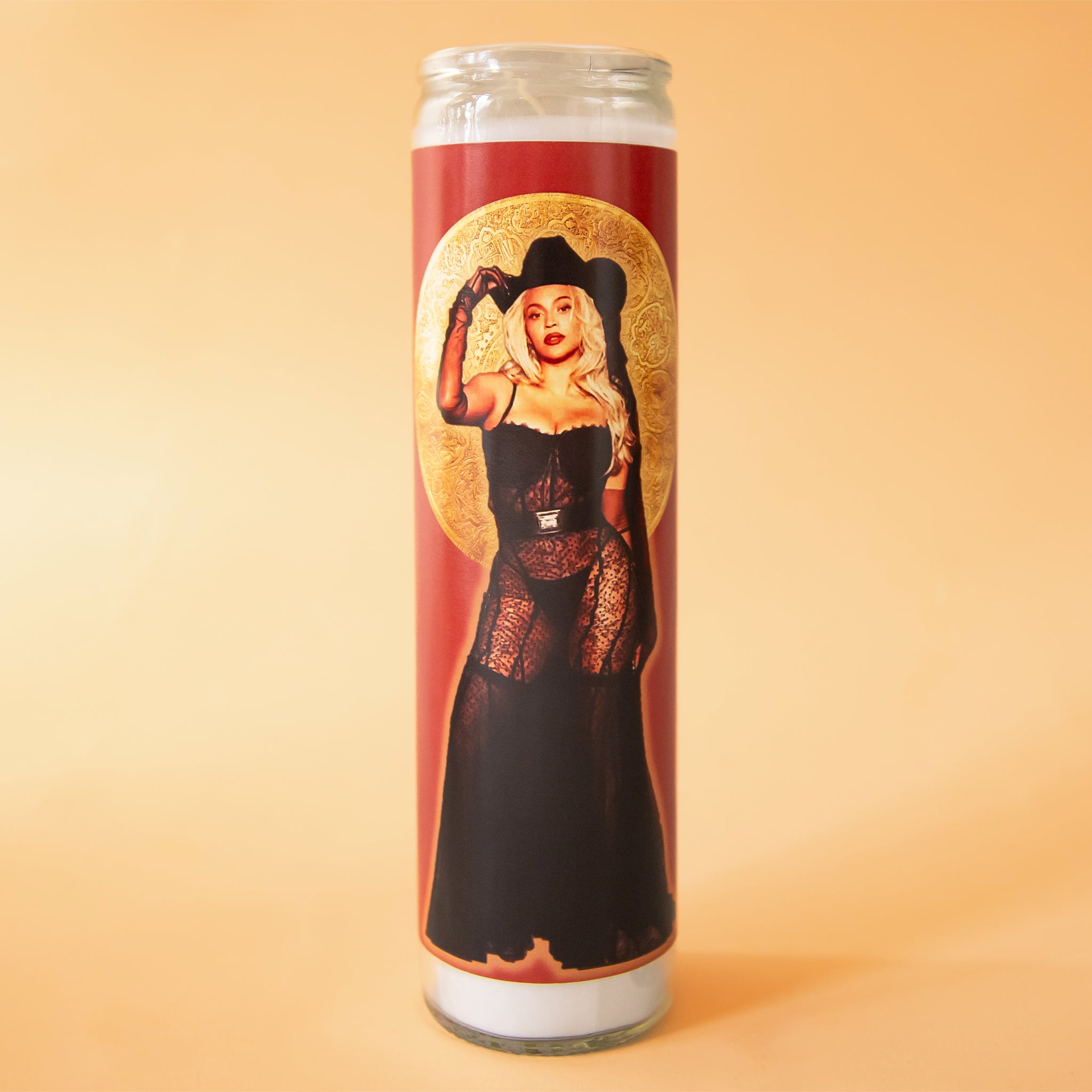 On a yellow background is a prayer candle with a label featuring a photo of Beyonce with a cowboy hat on. 