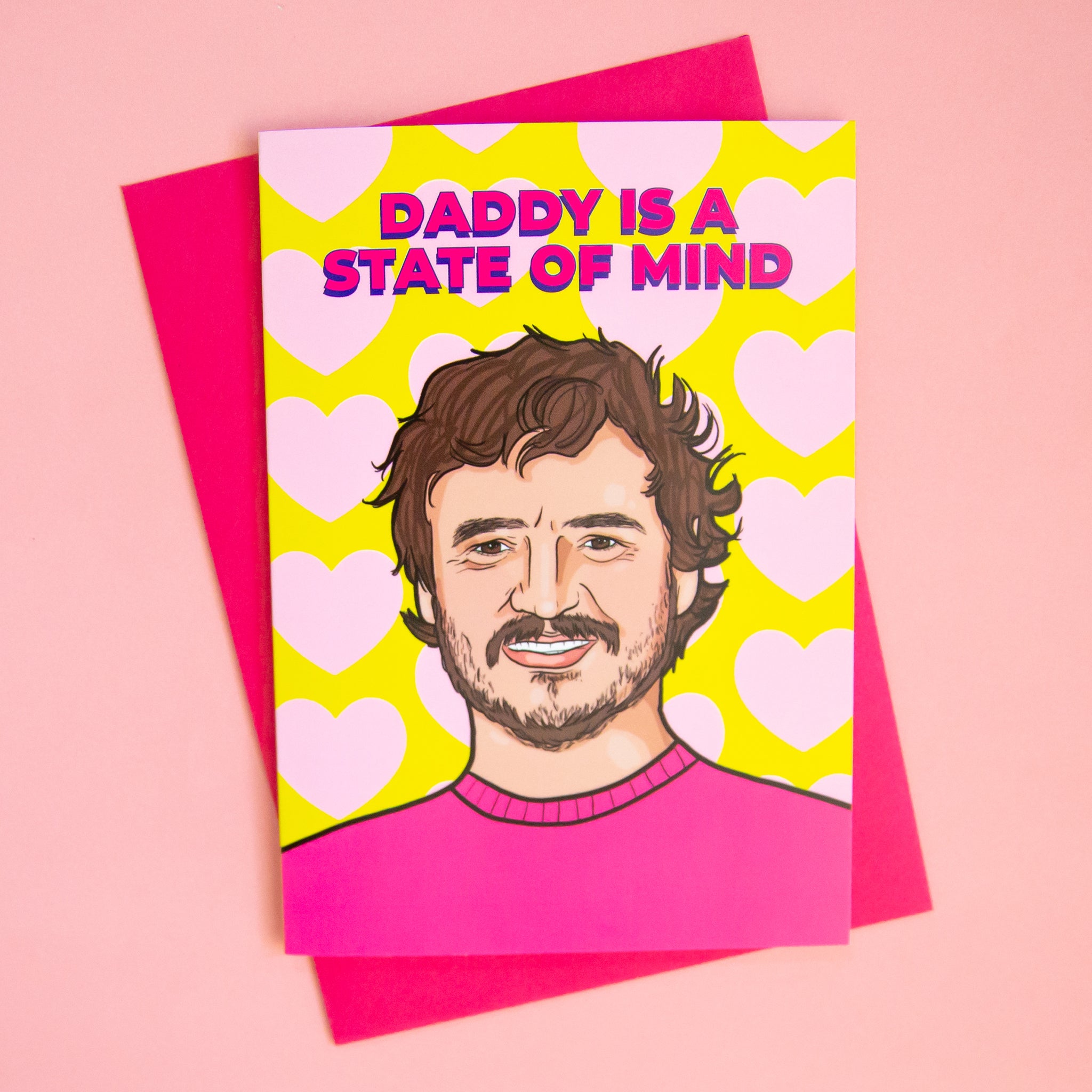 On a pink background is a card with an illustration that looks like Pedro Pascal and text above that reads, &quot;Daddy Is A State Of Mind&quot;. 