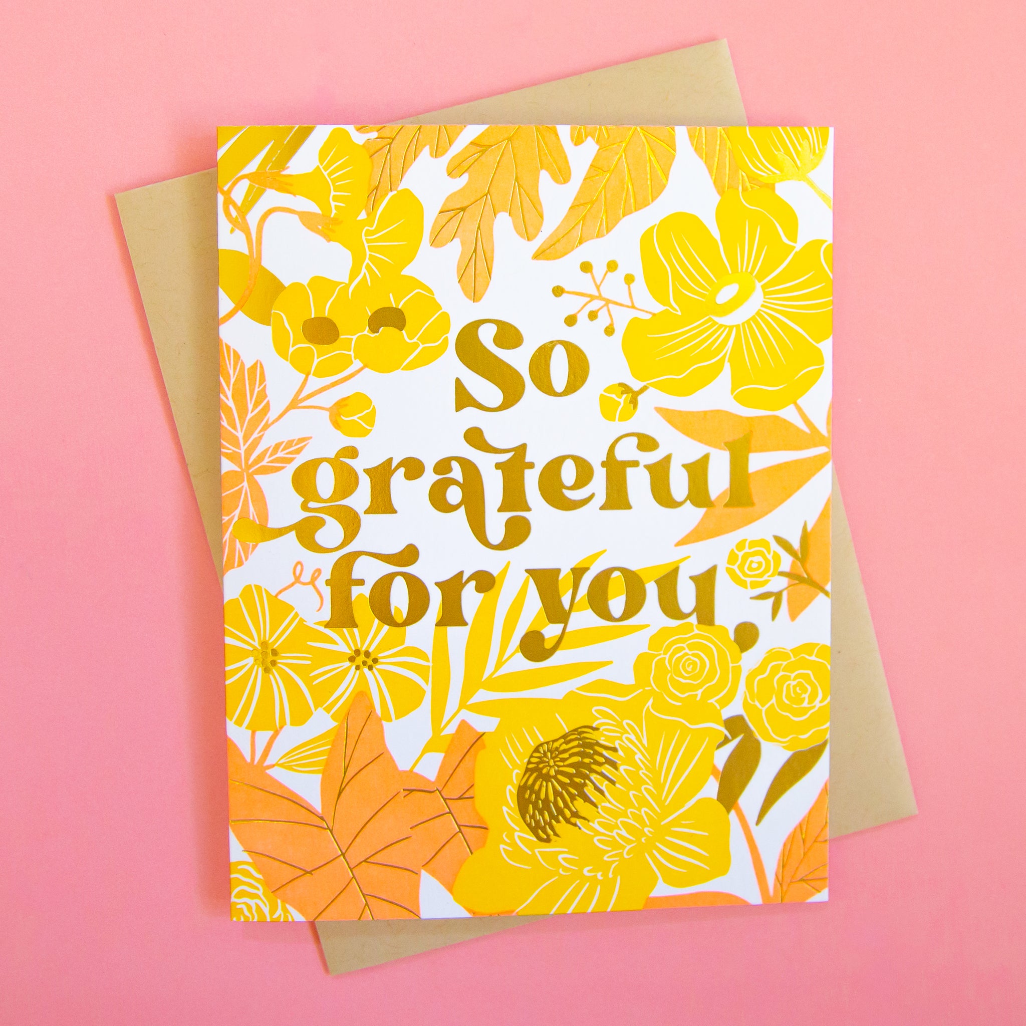 On a pink background is a yellow and pink floral card with gold foiled text that reads, &quot;So grateful for you&quot;.