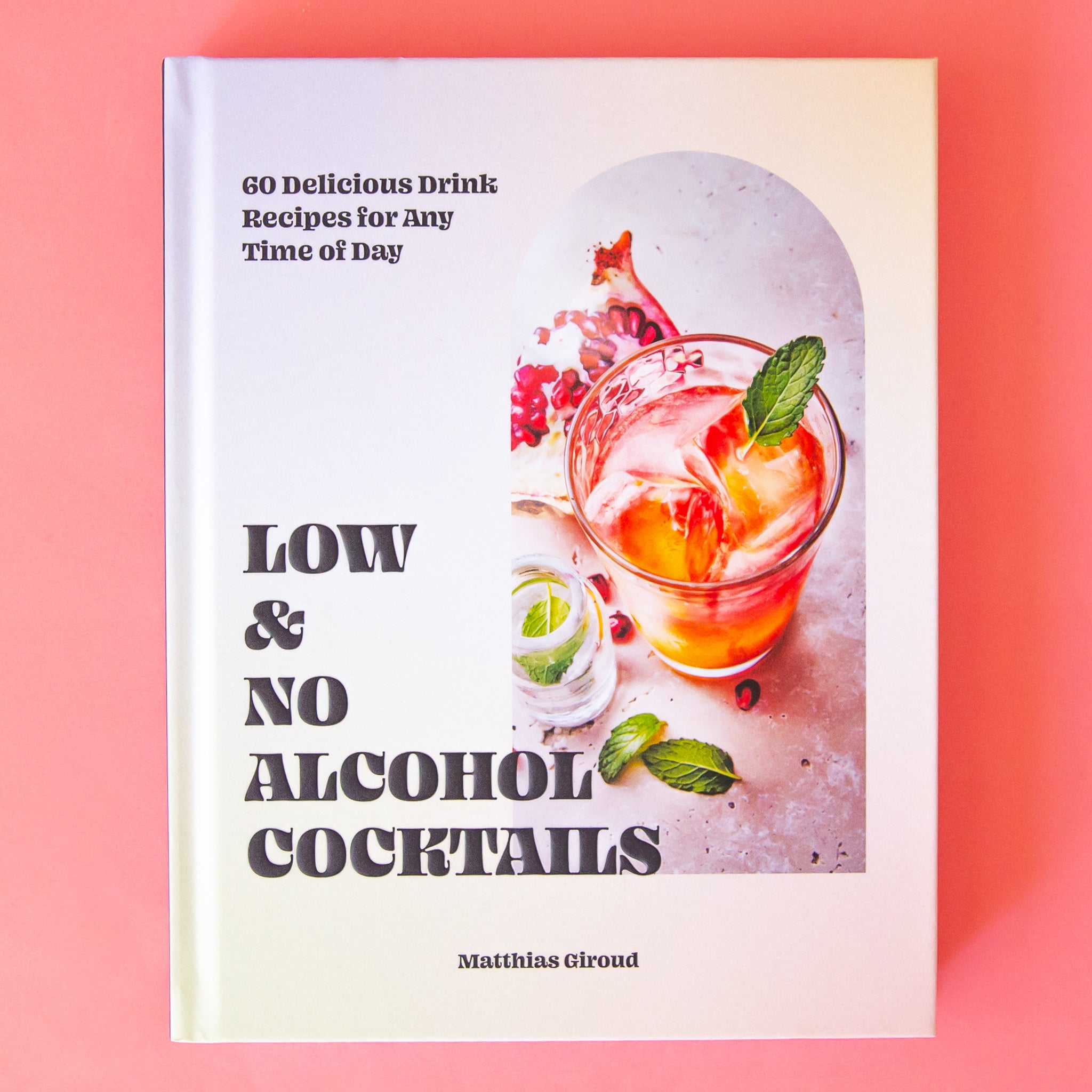On a pink background is a white book with a photo of a cocktail and black text that reads, "Low & No Alcohol Cocktails". 