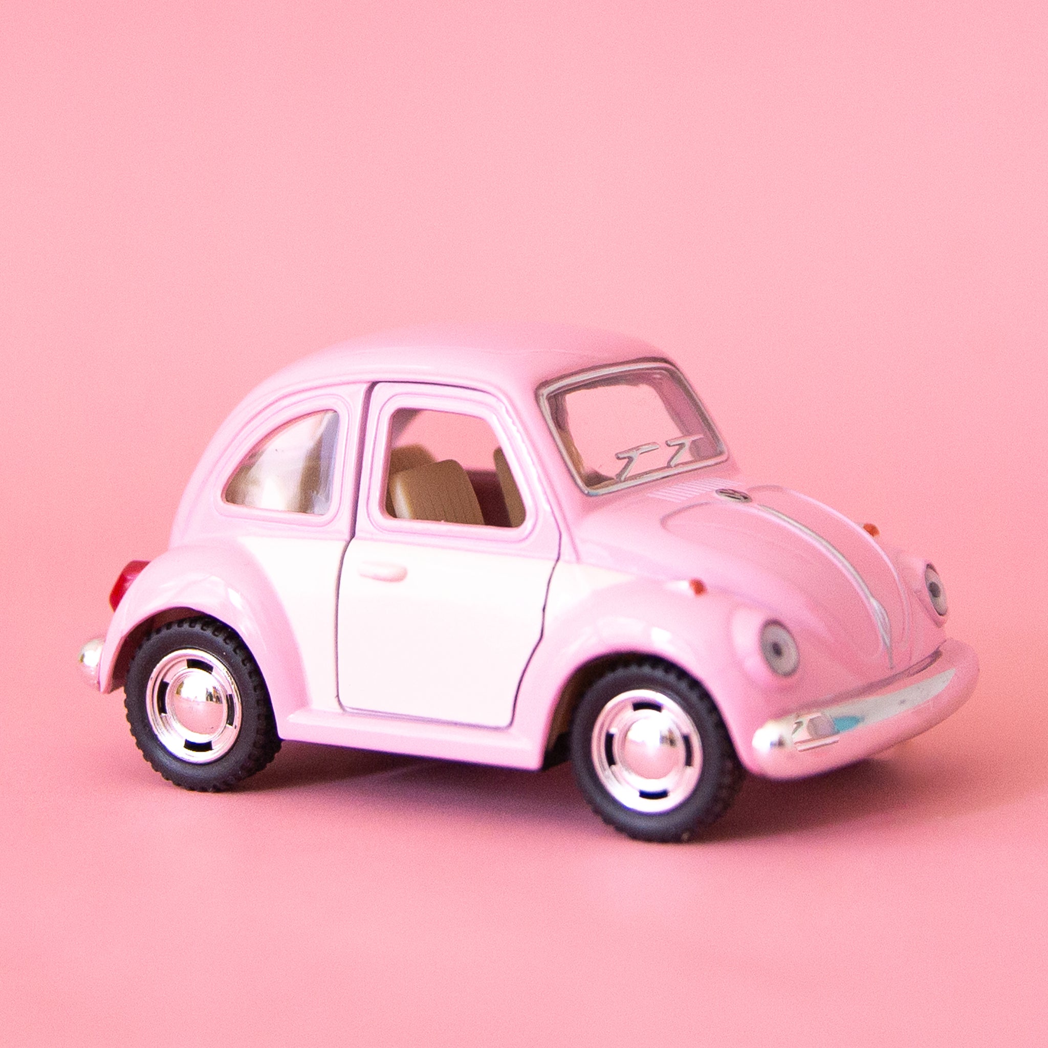On a pink background is a pink and white two toned toy in the shape of a volkswagen beetle. 