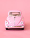 On a pink background is a pink and white two toned toy in the shape of a volkswagen beetle.