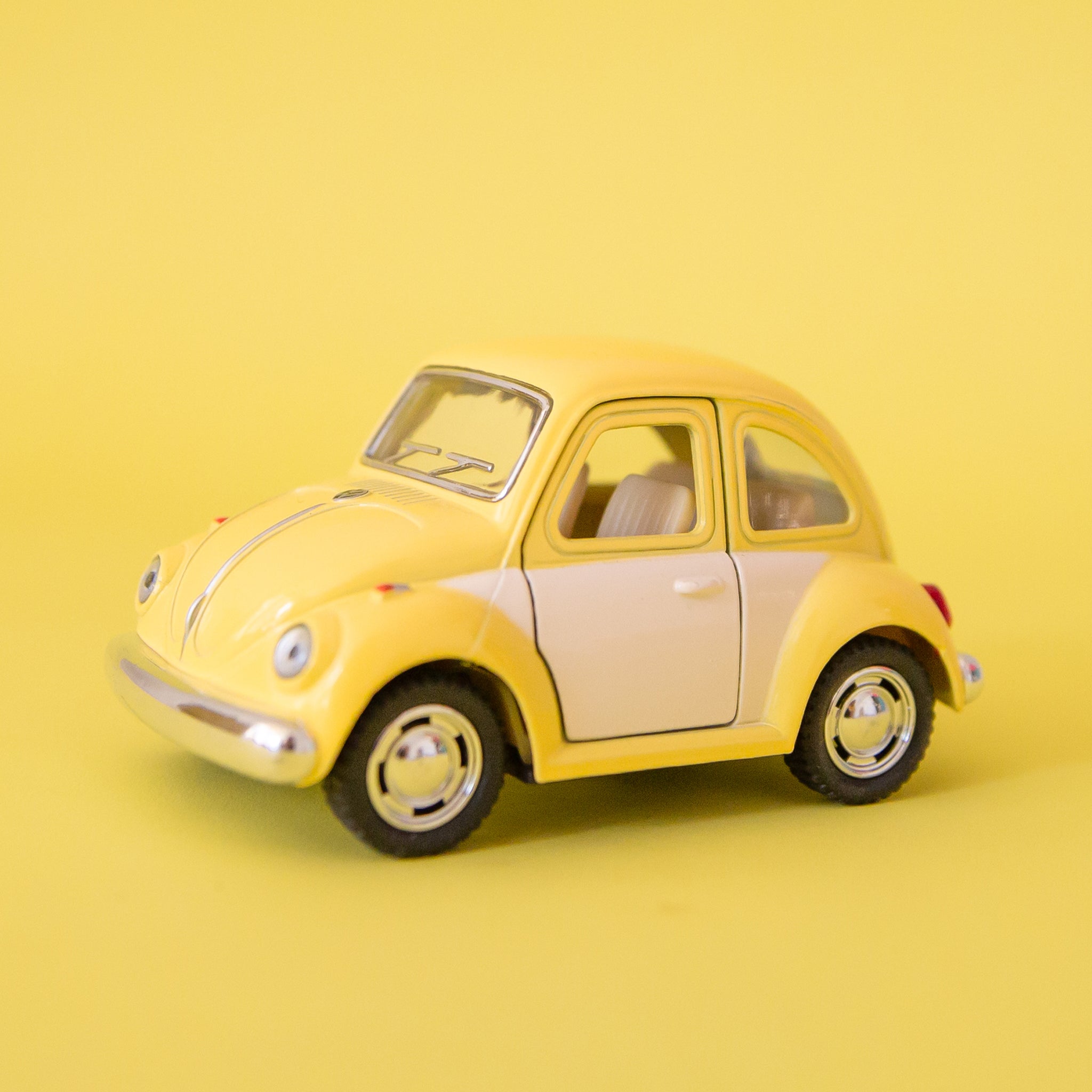 A yellow and white metal toy car volkswagen beetle.