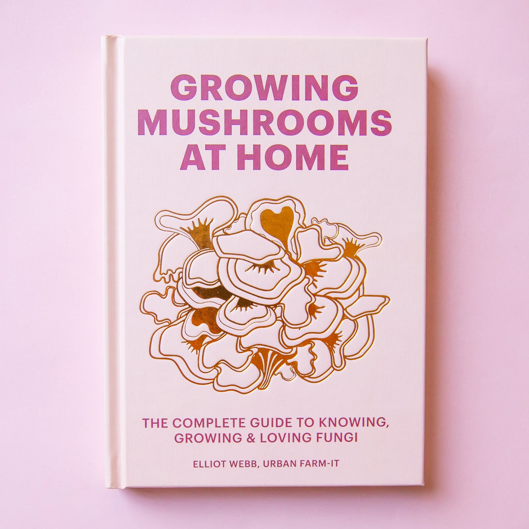 On a light purple background is a book cover with purple title that reads, "Growing Mushrooms At Home" along with a graphic of mushrooms in the center. 