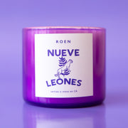 A purple glass candle with a white label with, "Nueve Leones".