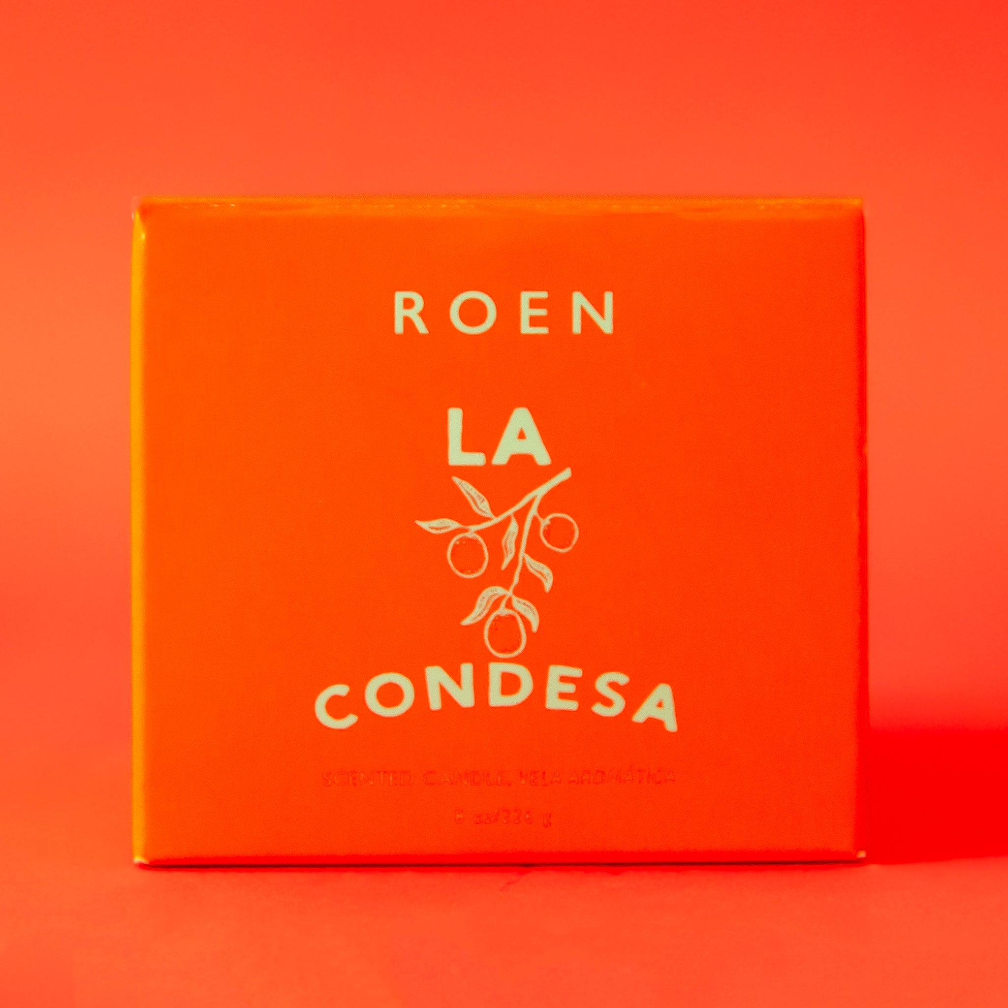 An orange/red glass jar candle with a label that reads, "La Condesa".