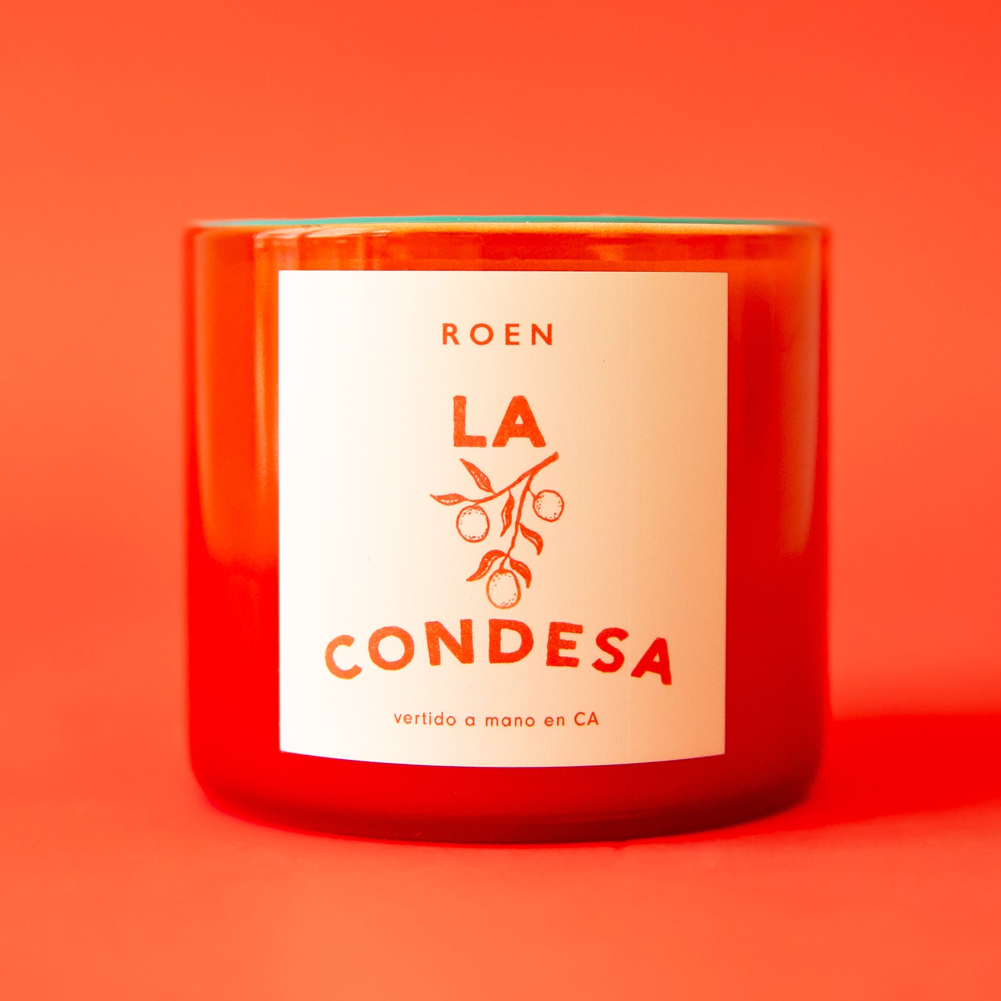 An orange/red glass jar candle with a label that reads, "La Condesa". 