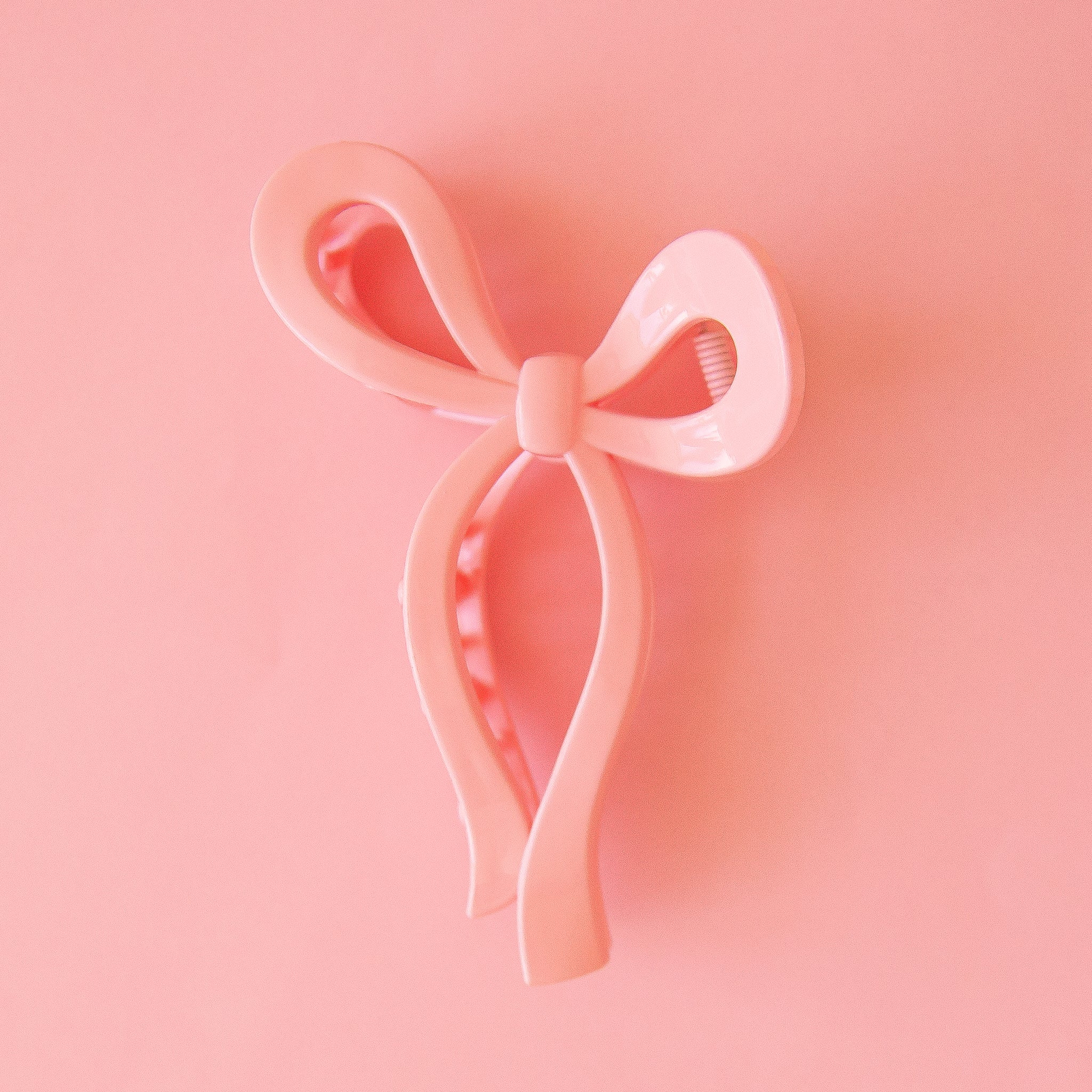 On a pink background is a pink knotted bow shaped hair clip.