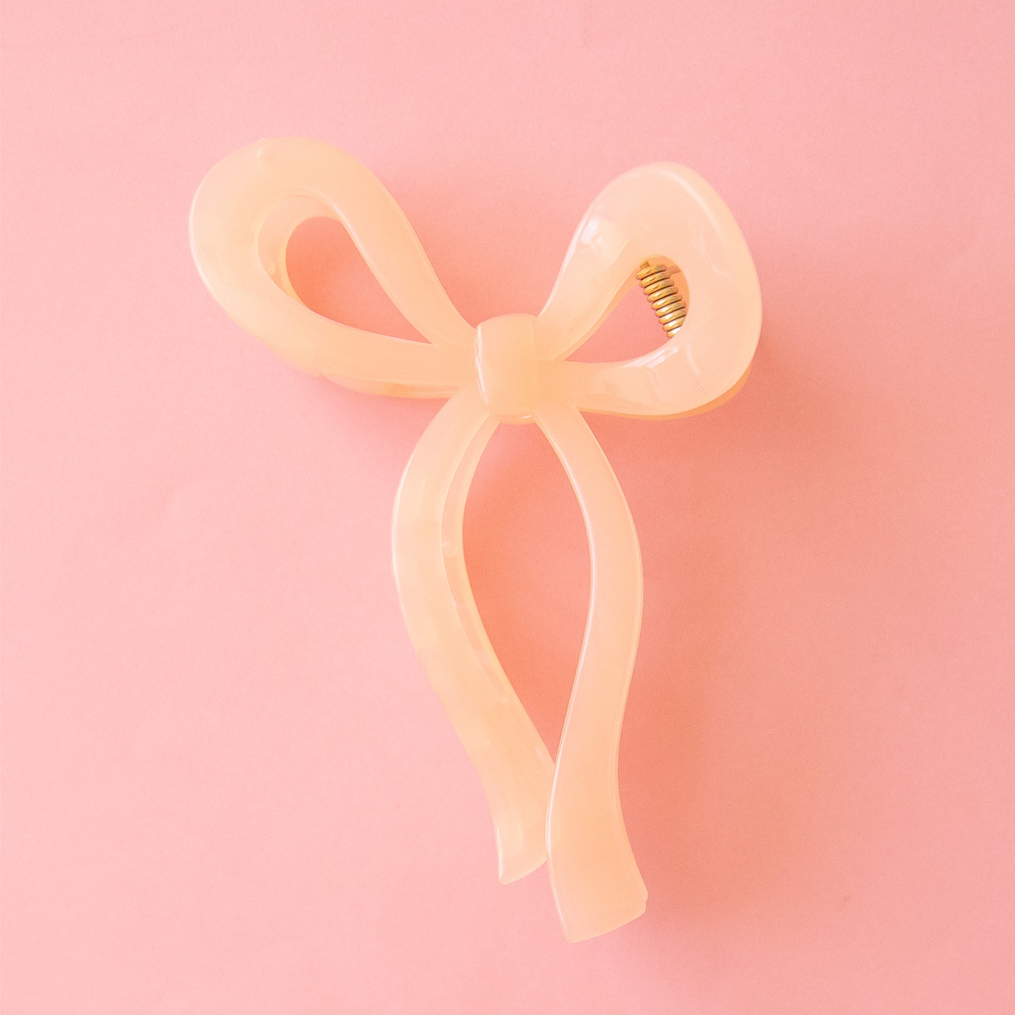 On a pink background is a transparent light pink hair clip in the shape of a knotted bow. 