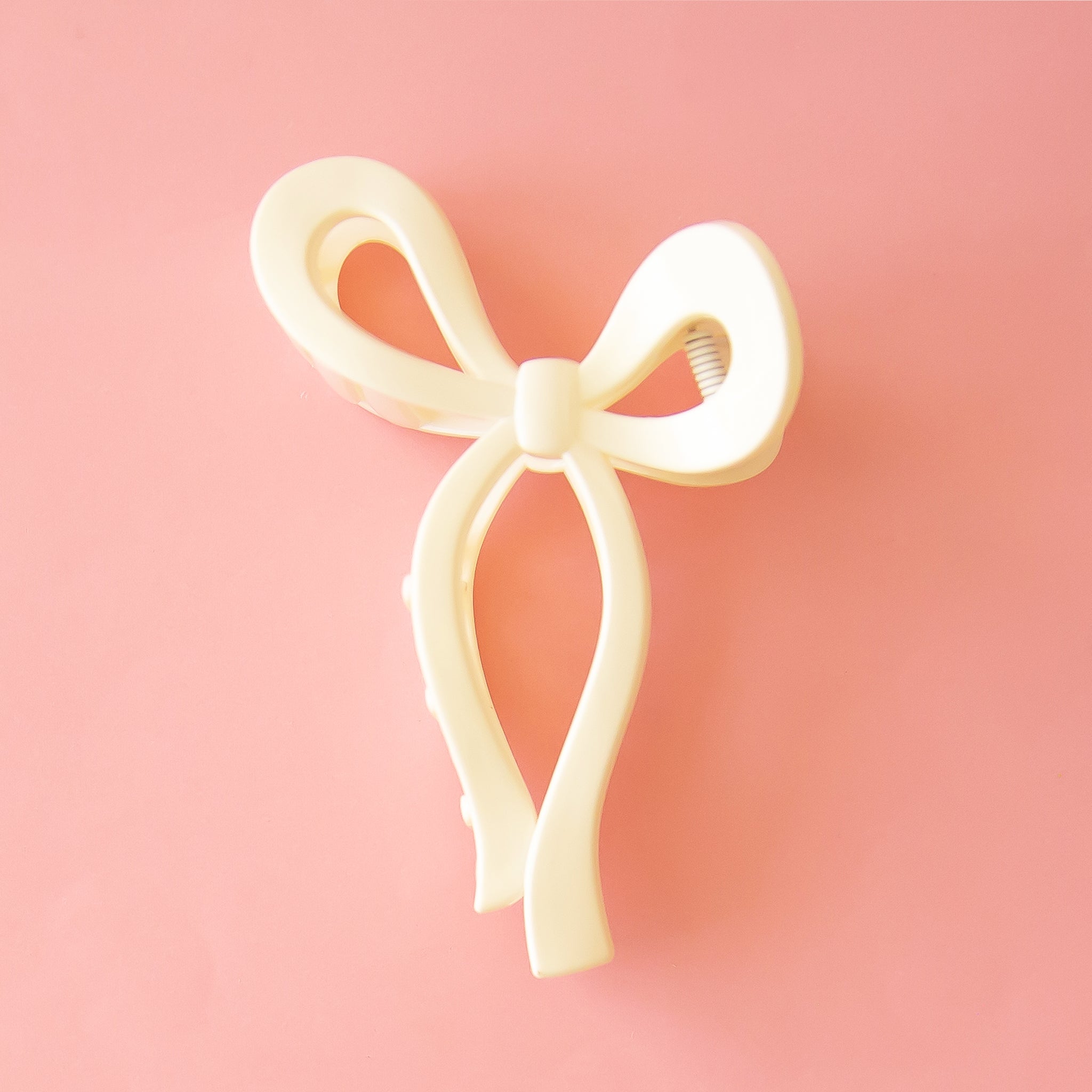 On a pink background is a white bow shaped hair clip. 