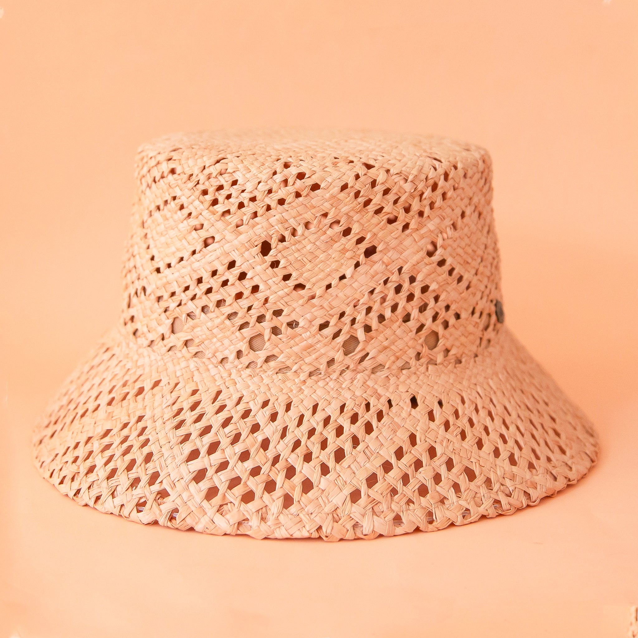 On a peachy background is a woven straw bucket hat. 