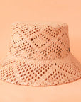 On a peachy background is a woven straw bucket hat.
