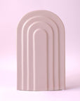 An arched ceramic vase in a cool toned pink shade.