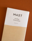 A rectangle chocolate bar packaged in a white and tan wrapper with black text that reads, "MAST Coffee Chocolate".