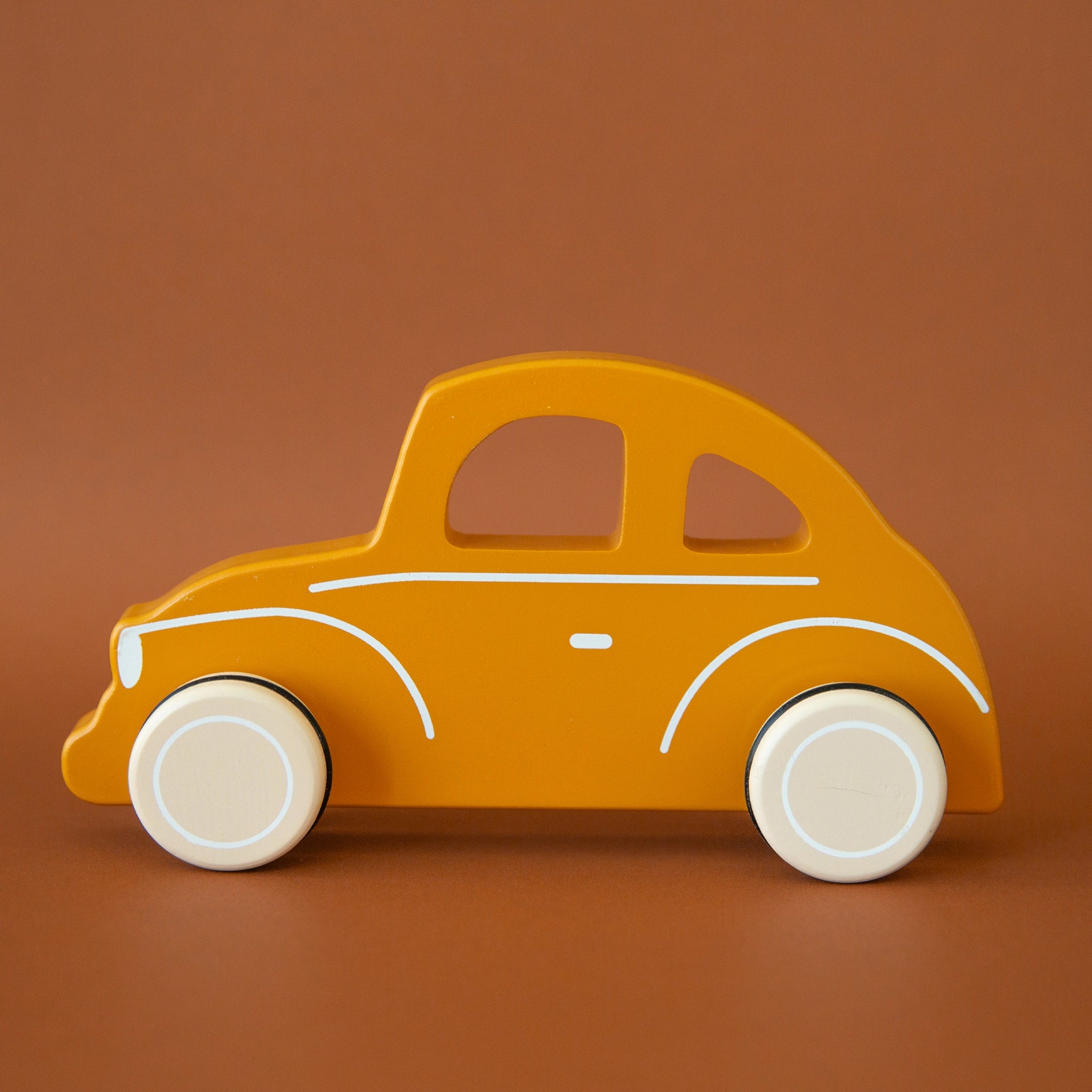 On a burnt orange background is a orange wood hand car toy with white wheels and accents. 