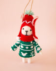 On a peachy background is a white felt dog ornament with a green sweater and red hat on.