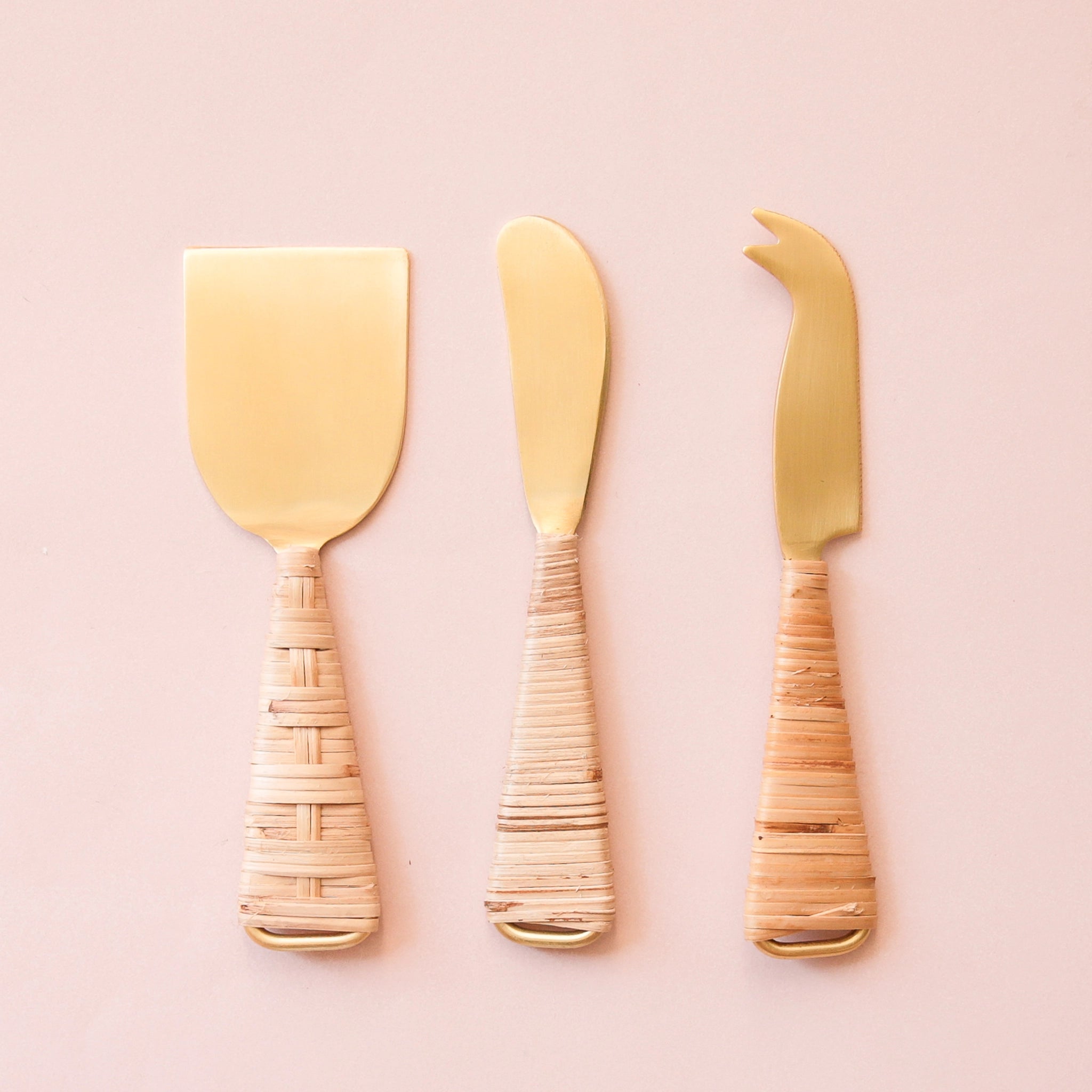 Gold cheese knives wrapped with natural rattan handles. A hatched design is on one side of the knives, while the opposite side is horizontally wrapped.