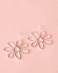 A pair of silver floral earrings lay on a pink ground