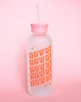 A glass water bottle with the word "HOWDY" in pink western style letters ,stacked five times at an angle on the front, a pink silicone lid with a straw coming out of the top.