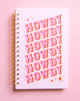 A light purple / cool toned pink notebook with the word "Howdy" slightly angled and stacked six times in pink western font and featuring a spiral bound detail.