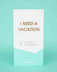 Eight white shower steaming tablets placed inside of a cardboard packaging that is teal blue and white and reads, "I Need A Vacation" in gold text.