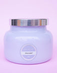 The larger of the two glass candle jars in a lavender purple shade along with a silver lid and a circle label in the center that reads, "Capri Blue, Volcano 06".