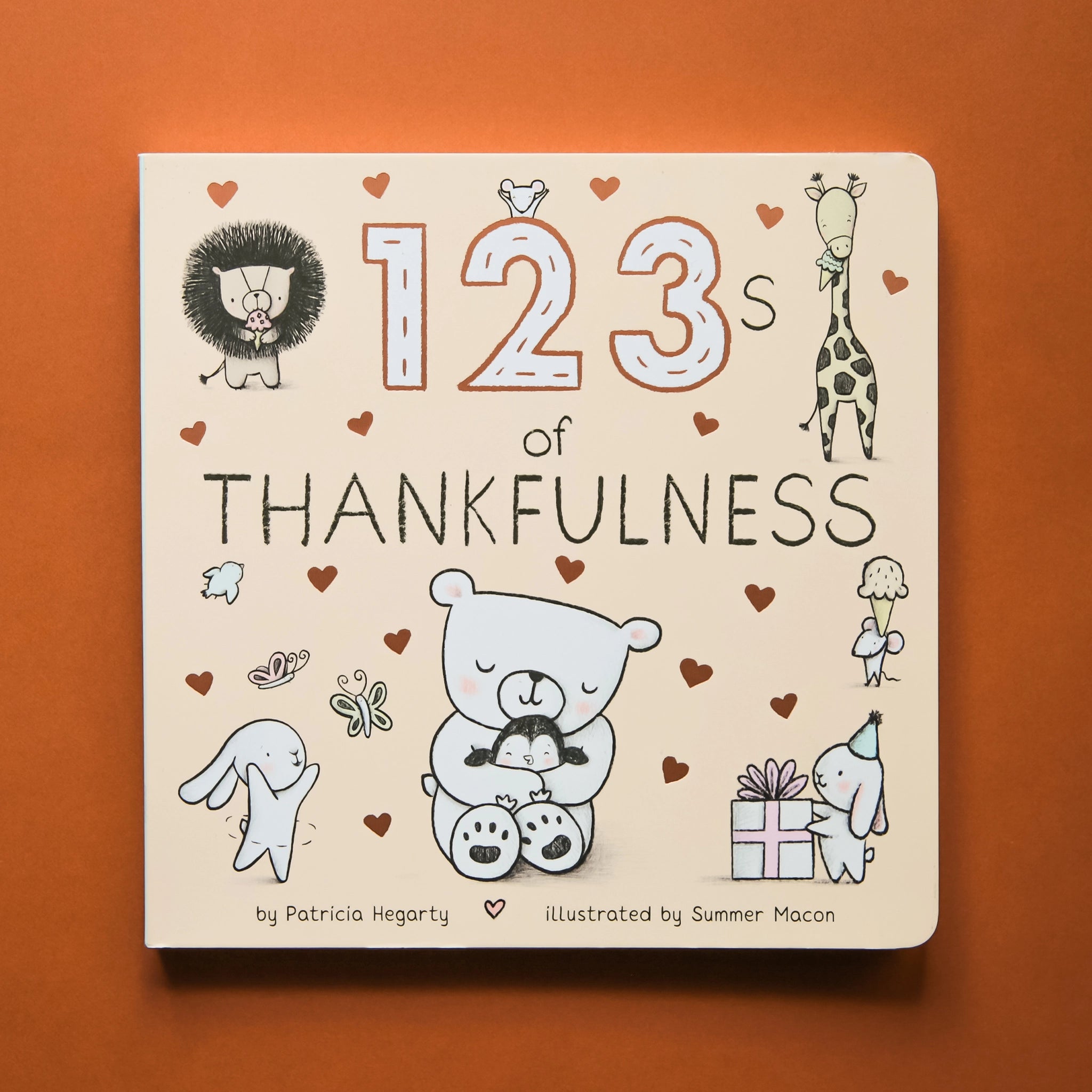 Small cream colored children's book titled "123's of Thankfulness" By Patricia Hegarty, Illustrated by Summer Macon. On the cover are illustrated gold hearts and black and white animals, including a lion, giraffe eating ice cream, mice, rabbits, and a bear hugging a baby penguin.