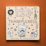 Small cream colored children's book titled "123's of Thankfulness" By Patricia Hegarty, Illustrated by Summer Macon. On the cover are illustrated gold hearts and black and white animals, including a lion, giraffe eating ice cream, mice, rabbits, and a bear hugging a baby penguin.