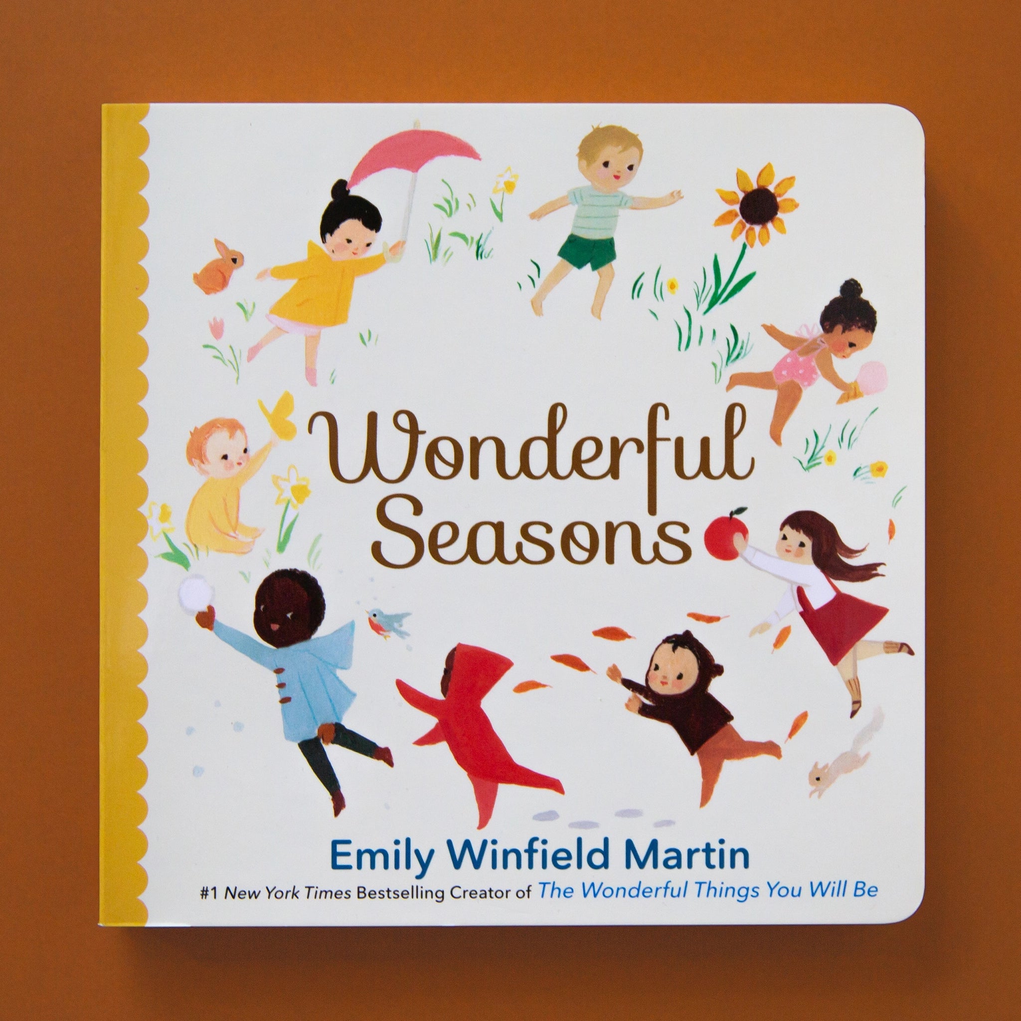 On a brown background is a white book cover with children in a circle around the book title that reads, "Wonderful Seasons" 
