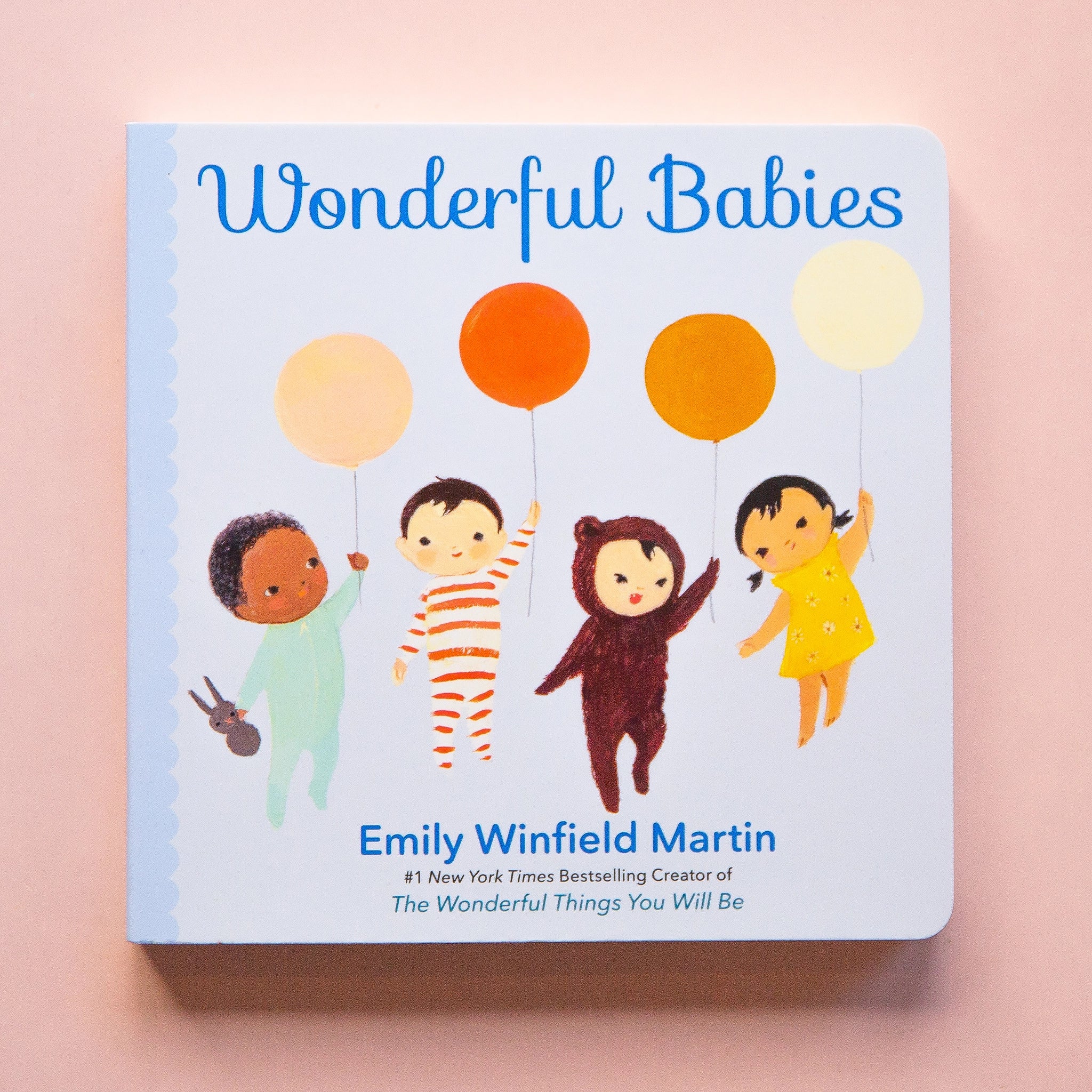 On a peachy background is a neutral book cover with four babies holding different colored balloons and the title across the top that reads, &quot;Wonderful Babies&quot;.