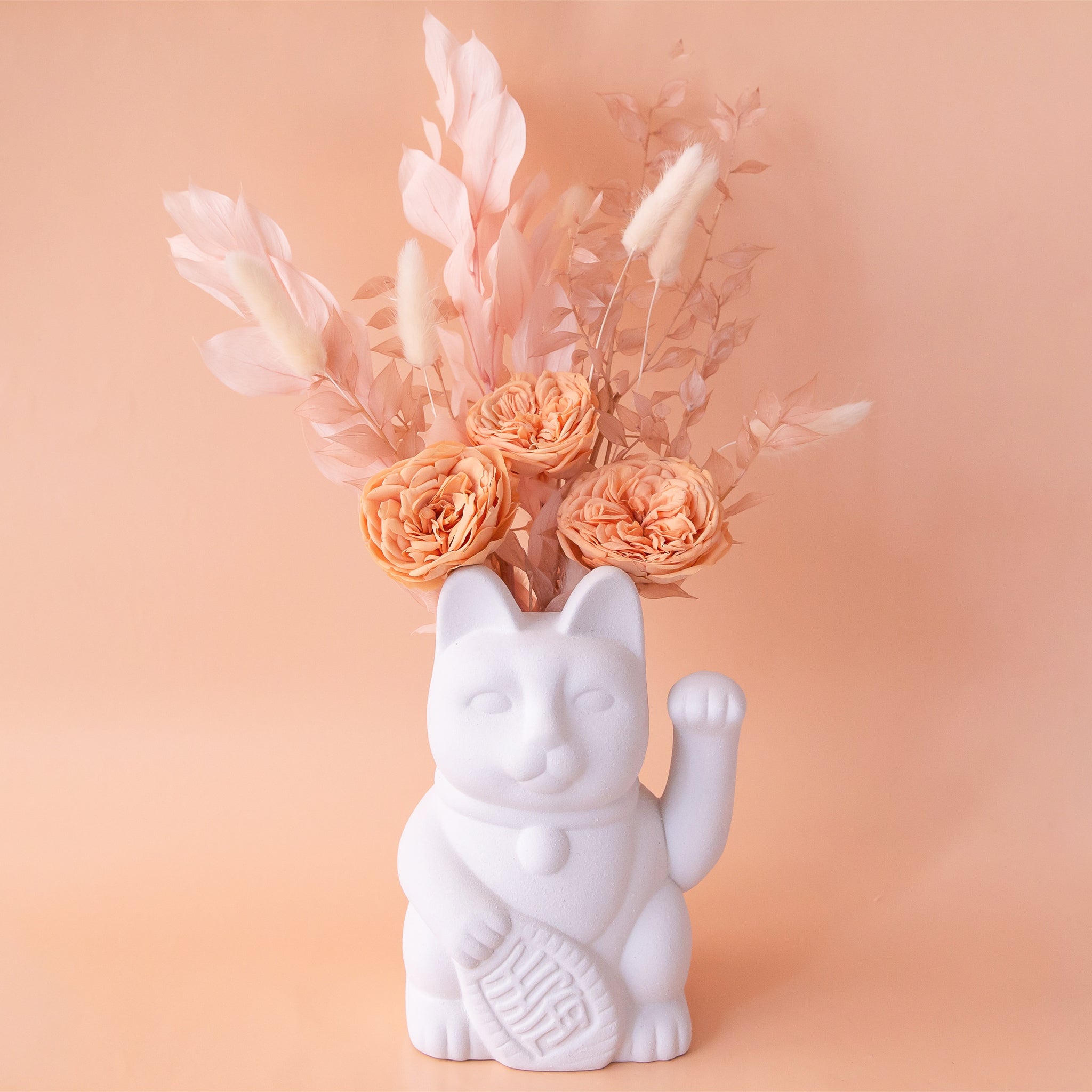 A ceramic lucky cat vase in white with its paw up in the waving position staged here with natural dried florals.