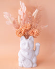 A ceramic lucky cat vase in white with its paw up in the waving position staged here with natural dried florals.