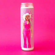 On a hot pink background is a prayer candle with a picture of margot robbie as Barbie wearing a bright pink cowgirl outfit.