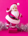 On a hot pink background is a hot pink flocked Santa shaped figurine holding a dancing pose.