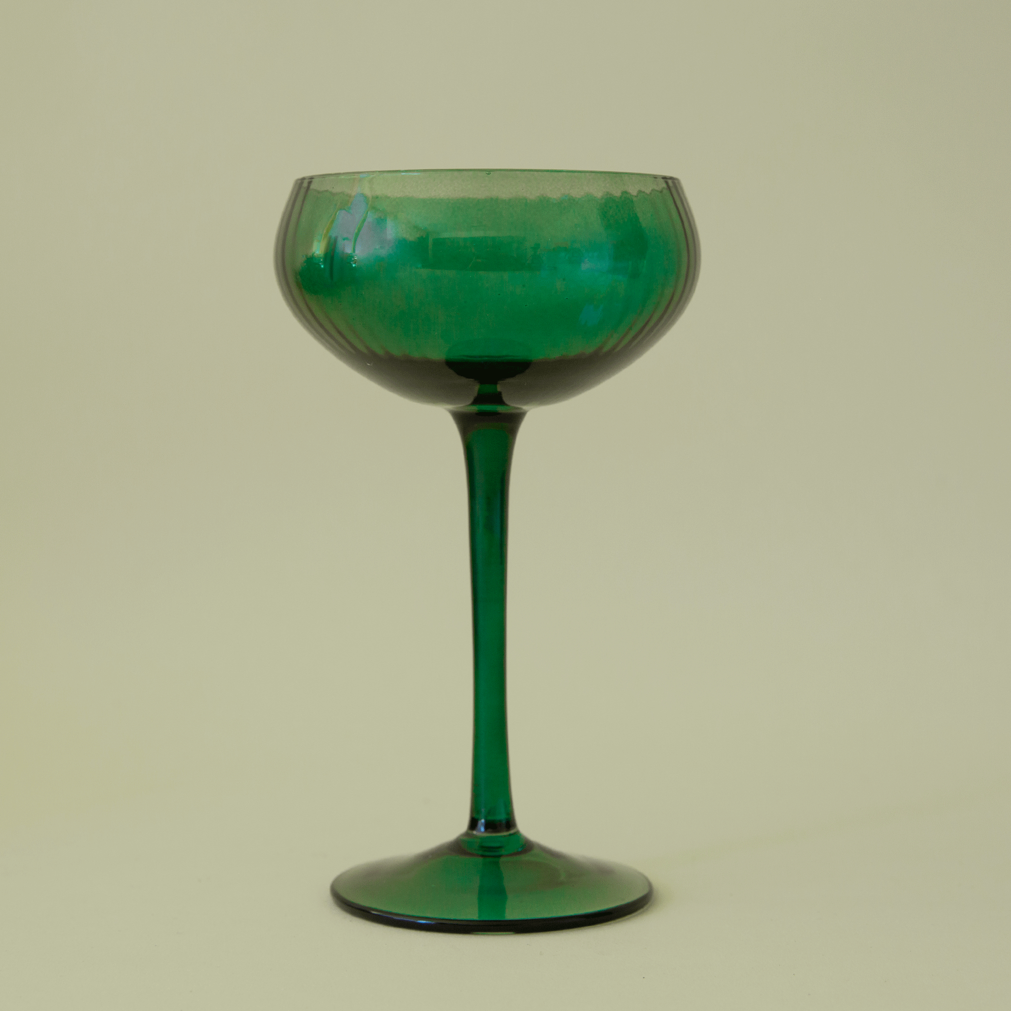 On a green background is a green glass coup glass with a subtle ribbed texture. 