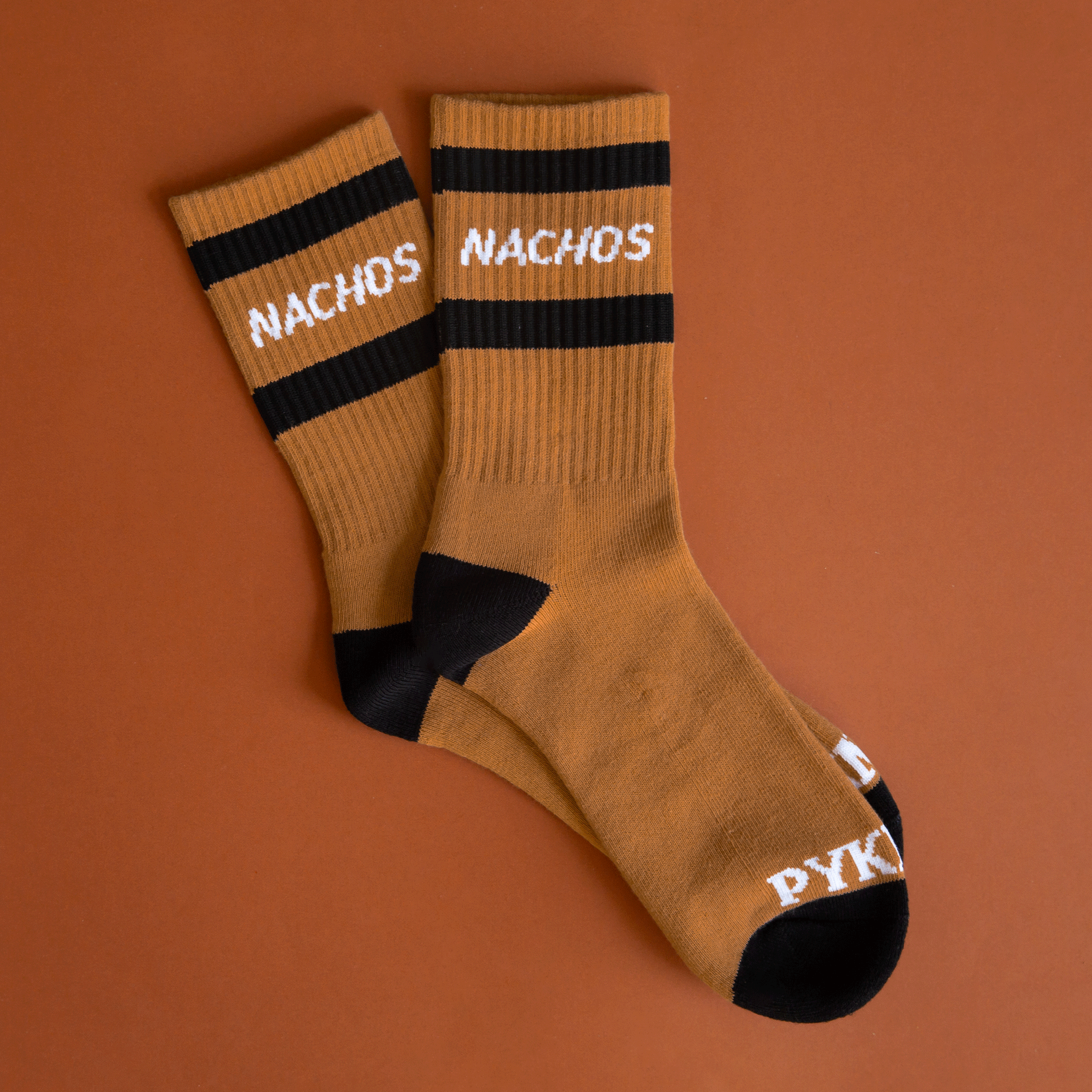 Tan crew socks with black detailing and two black stripes across the top and says "Nachos" in white text.